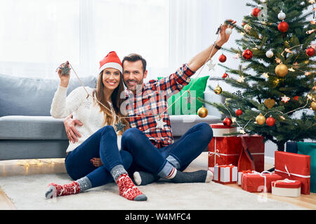 Photo of cheerful couple holding christmas decorations and sitting in living room having fun Stock Photo