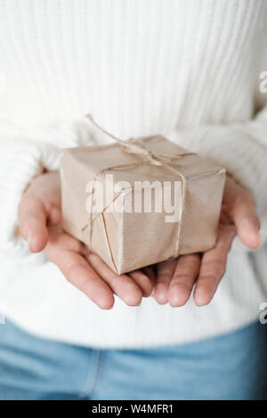 Woman in white knitted sweater giving wrapped gift.  Close up Female hands holding Christmas box present. Christmas, New Year, shopping, preparation o Stock Photo