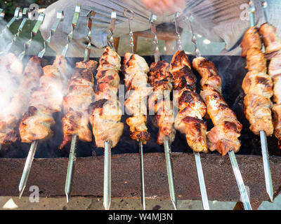 man cooks skewered shish kebabs (shashlyk) from pork meat on brazier outdoors Stock Photo