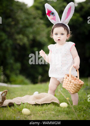 1-year-old toddler in Easter Bunny costume collecting eggs outside Stock Photo