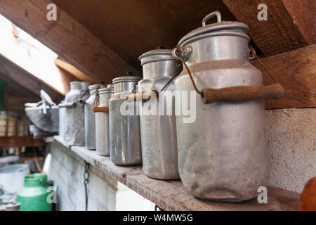 Old aluminum milk churns on a shelf under the roof. Stock Photo