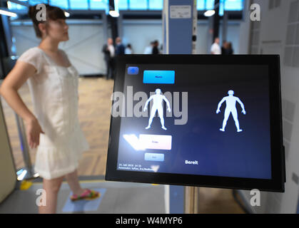 24 July 2019, Hessen, Frankfurt/Main: A woman is standing in a body scanner in a newly constructed hall in Terminal 1 of Frankfurt Airport. The seven new control lanes are intended to ensure smoother operation. Thanks to a new configuration, more passengers per hour can be guided through than with the technology previously used. Photo: Arne Dedert/dpa Stock Photo