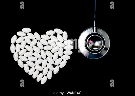 Heart shape made of white pills on black background and stethoscope Stock Photo