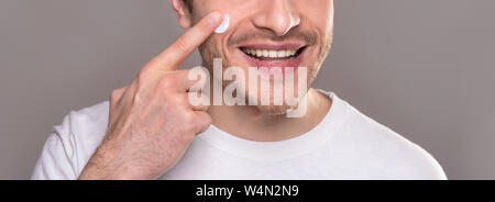 Smiling man moisturizing face with crea,. close up portrait Stock Photo