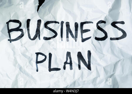 Phrase "business plan" handwritten on crumpled torn paper. Sign, concept of failed plans or poor management, abstract illustrative image Stock Photo