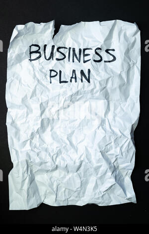 Phrase 'business plan' handwritten on crumpled torn paper, top view. Sign, concept of failed plans or poor management, abstract illustrative image Stock Photo