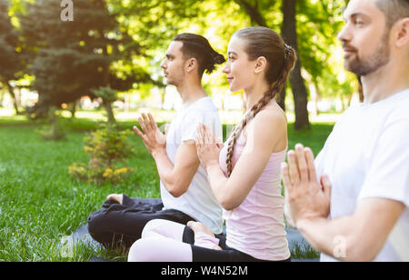 Three friends holding hands in namaste while practicing yoga outdoors Stock Photo