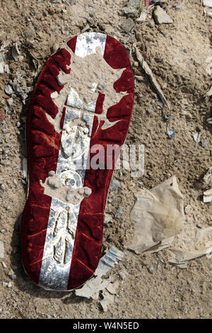 The flag of Latvia is depicted on the sole of an old boot. Ecology concept with environmental pollution from household and industrial waste. Stock Photo