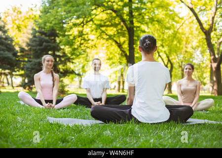 Young smiling people practicing yoga lesson with instructor in park Stock Photo