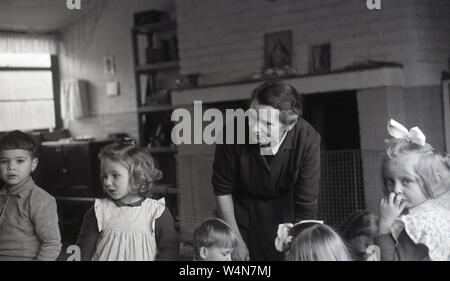 1950s, historical, female teacher with young children in a room inside a small village nursery, England, UK. Stock Photo