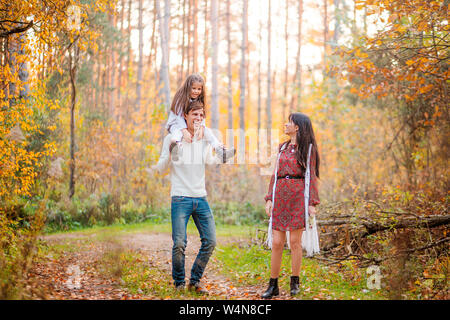 Photo of Mom, dad and daughter walk through the autumn forest. Daughter sits on father's shoulders Stock Photo