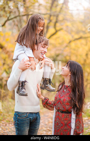 Photo of Mom, dad and daughter walk through the autumn forest. Daughter sits on father's shoulders Stock Photo