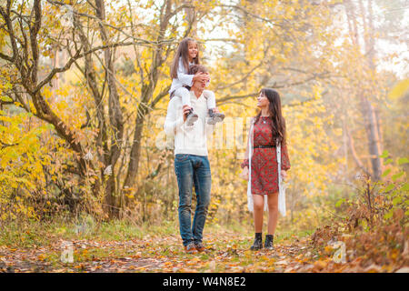 Photo of Mom, dad and daughter walk through the autumn forest. Daughter sits on father's shoulders Stock Photo