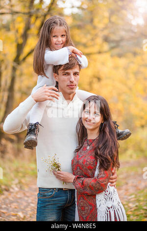 Photo of Mom, dad and daughter walk through the autumn forest. Daughter sits on father's shoulders Stock Photo