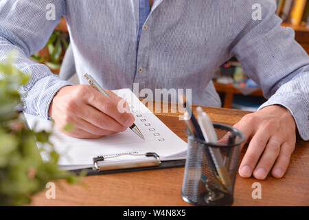 Man filling out a questionnaire on a wooden table. Horizontal composition. Elevated view. Stock Photo