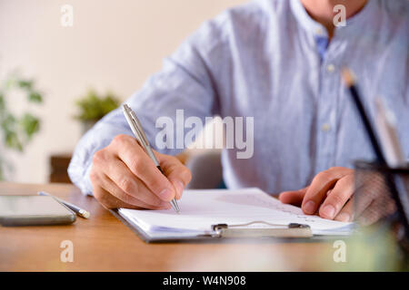 Man filling out a questionnaire on a wooden table. Horizontal composition. Front view. Stock Photo