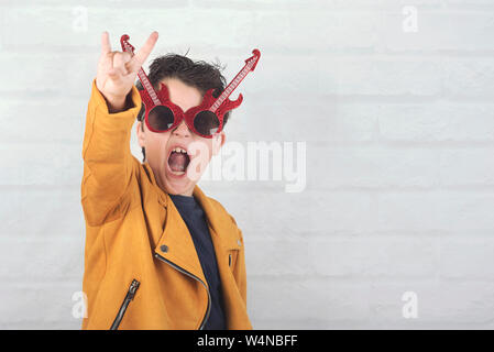 child with sunglasses doing rock symbol with hands up against brick background Stock Photo