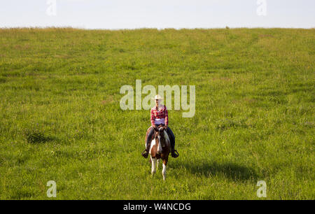 A young girl rides a horse on a pasture near a ranch Stock Photo