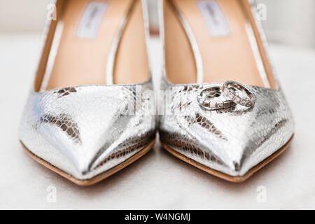 Closeup of the brides silver shoes toes and wedding rings on the marble floor, selective focus Stock Photo