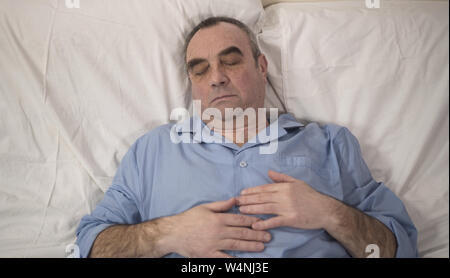 Handsome senior man waking up in good mood at home after nice calm night. Happy male pensioner smiling lying in bed, sleeping on comfortable mattress Stock Photo