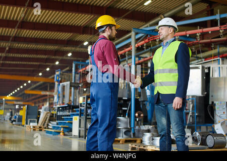 Two engineers in the uniform and helmets shaking each others hands as if coming to an agreement in something. Stock Photo