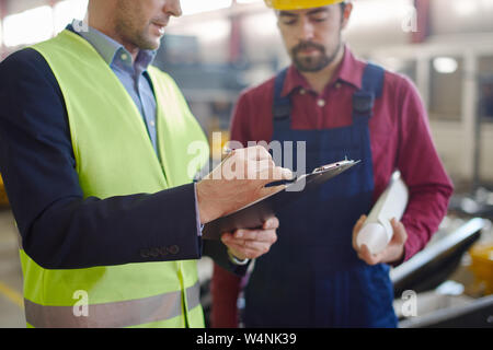 Two engineers in the uniform working on some paperwork involving blueprints and notepads with additional information to the project. Stock Photo
