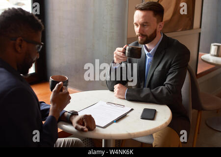 Two men drinking tea poured from a glass pot and having a conversation with each other in a pleasant atmosphere. Stock Photo