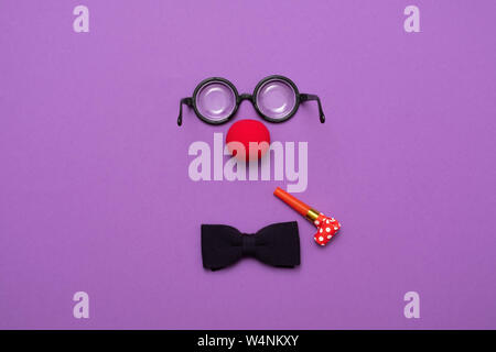 Funny glasses, red clown nose and tie lie on a colored background, like a face. Stock Photo