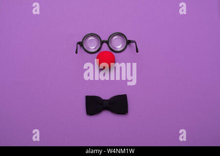 Funny glasses, red clown nose and tie lie on a colored background, like a face. Stock Photo