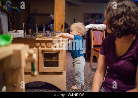 a toddler busily plays with a toy kitchen while his mother looks on Stock Photo