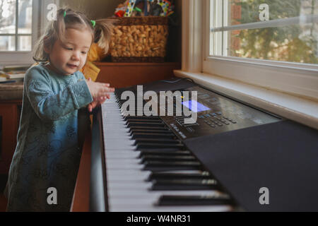 a cute little girl in pigtails plays on a keyboard in front of window Stock Photo