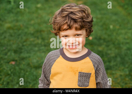 a smiling curly-haired boy stands in a grassy field Stock Photo
