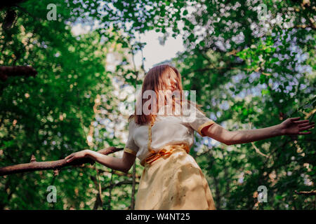 woman standing on a tree in a yellow dress Stock Photo