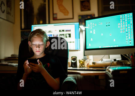 Kid sitting at desk using smart phone Stock Photo