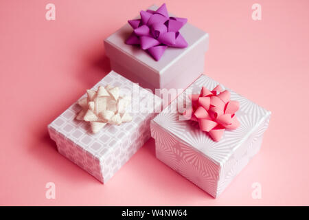 Three light gray gift boxes with colorful bows on pink background. Festive concept. Stock Photo