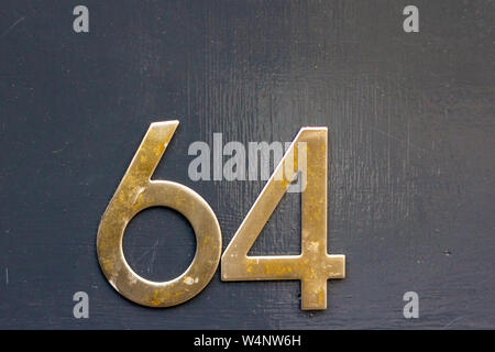 House number 64 with the sixty four in bold brass digits on a black shiny surface Stock Photo