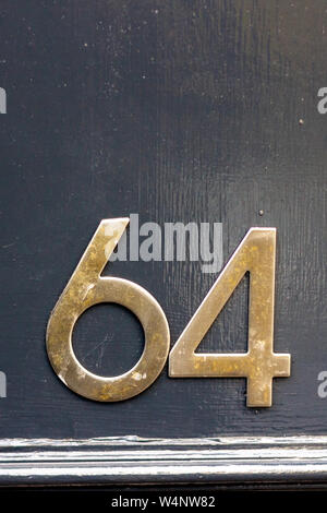 House number 64 with the sixty four in bold brass digits on a black shiny surface Stock Photo