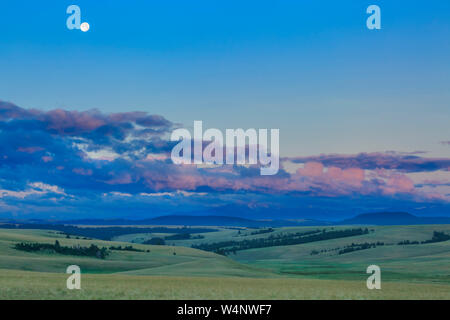 full moon setting above peaks of the flint creek range and the snowshoe creek basin near avon, montana Stock Photo