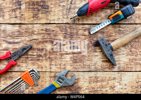 Old hand tools, pliers, hammer, tape measure, adjustable wrench, electric screwdriver, a set of hex keys lie on the old wooden table. Stock Photo