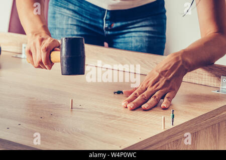 Female hands assembling new furniture and using a rubber hammer. Stock Photo