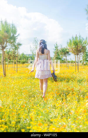 Rear view of a beautiful woman in dress walking through a field of flowers carrying her shoes