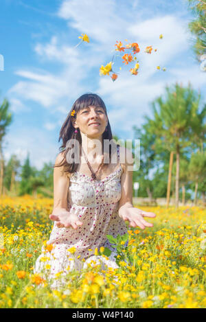 Beautiful woman in dress sitting on a meadow while throwing flowers Stock Photo