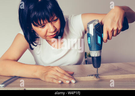 Woman assembling new furniture and using a cordless drill. Stock Photo