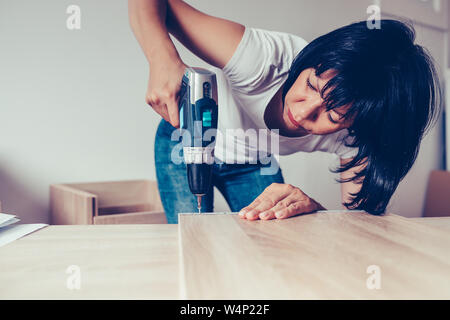 Woman assembling new furniture and using a cordless drill. Stock Photo