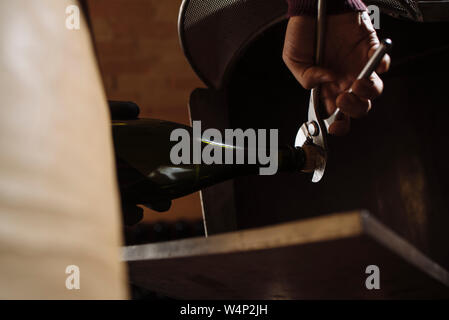 Crop male worker opening cork of Cava sparkling wine with pliers in Penedes region, Catalonia, Spain Stock Photo