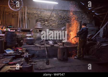 young traditional Blacksmith working with open fire  The blacksmith making flames in smithy with spark fireworks forging hot iron in workshop Stock Photo
