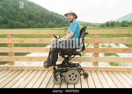 disabled happy young man in electric wheelchair on a boardwalk enjoying his freedom and smiling Stock Photo