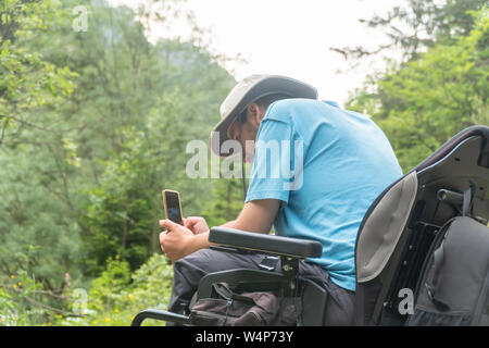 man on electric wheelchair using smartphone camera in nature Stock Photo