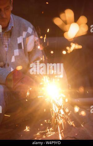 the blacksmith polishing metal products making sparks while using a grinding machine in his traditional workshop Stock Photo