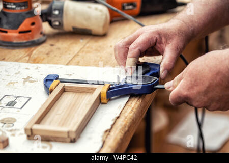 Close-up senior carpenter glueing wooden craft surface and joining with clamps. Woodwork carpenter with equipment and tools at workshop. Handmade diy Stock Photo
